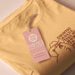 A yellow crew neck short sleeve t-shirt, with an embroidered brown thread design of a cute singing cat wearing a cowboy hat and the song lyric country roads, take me home to the place I belong