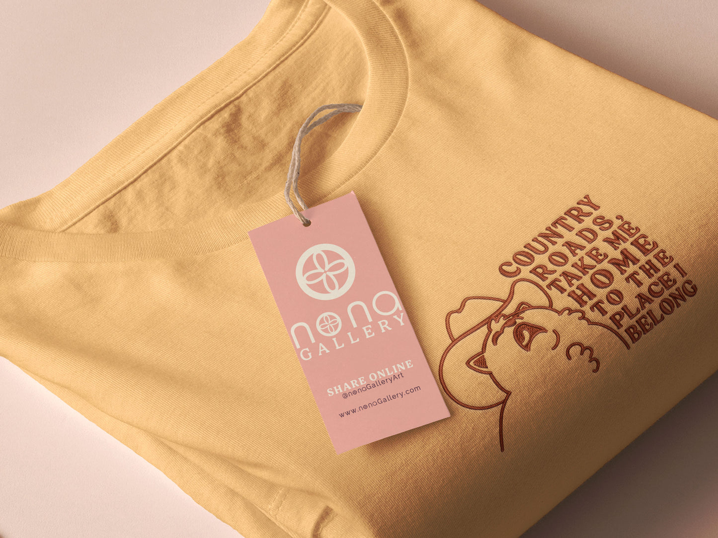 A yellow crew neck short sleeve t-shirt, with an embroidered brown thread design of a cute singing cat wearing a cowboy hat and the song lyric country roads, take me home to the place I belong