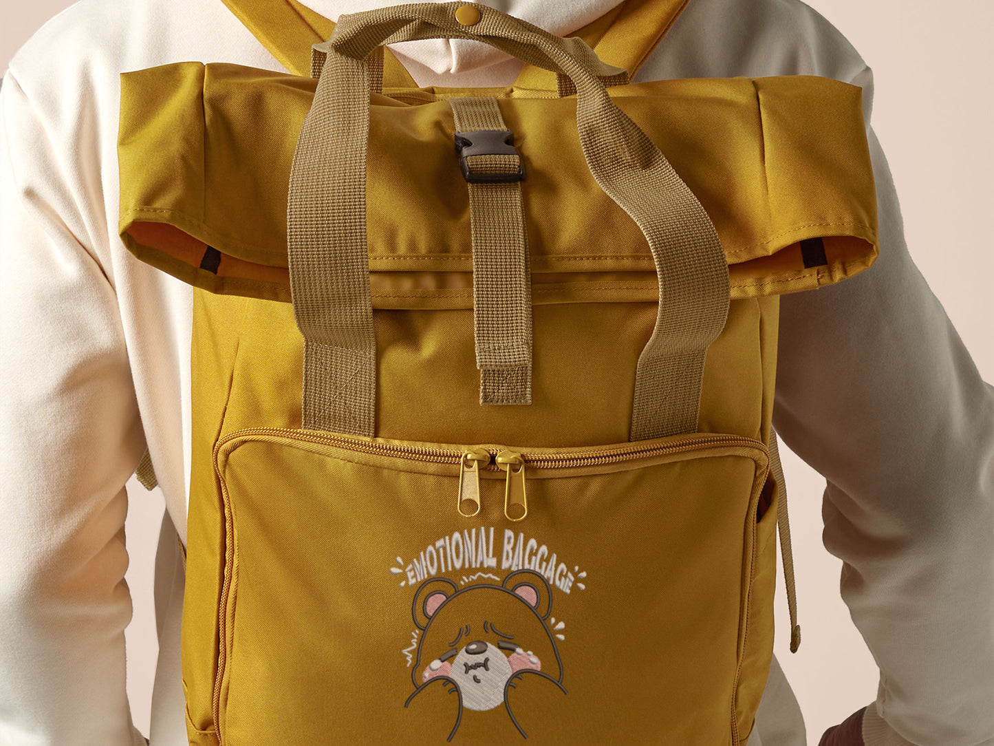 Yellow roll top twin handle backpack with an embroided design of cute crying bear and the quote emotional baggage