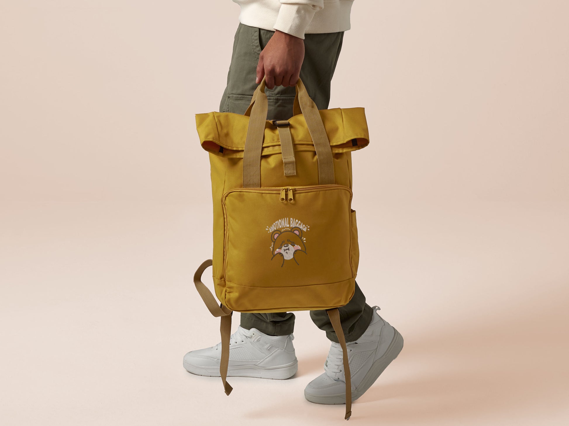 Yellow roll top twin handle backpack with an embroided design of cute crying bear and the quote emotional baggage
