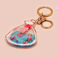A large transparent acrylic shaker keychain with gold keyring, filled with mini chibi shrimps and labelled as emotional support shrimp