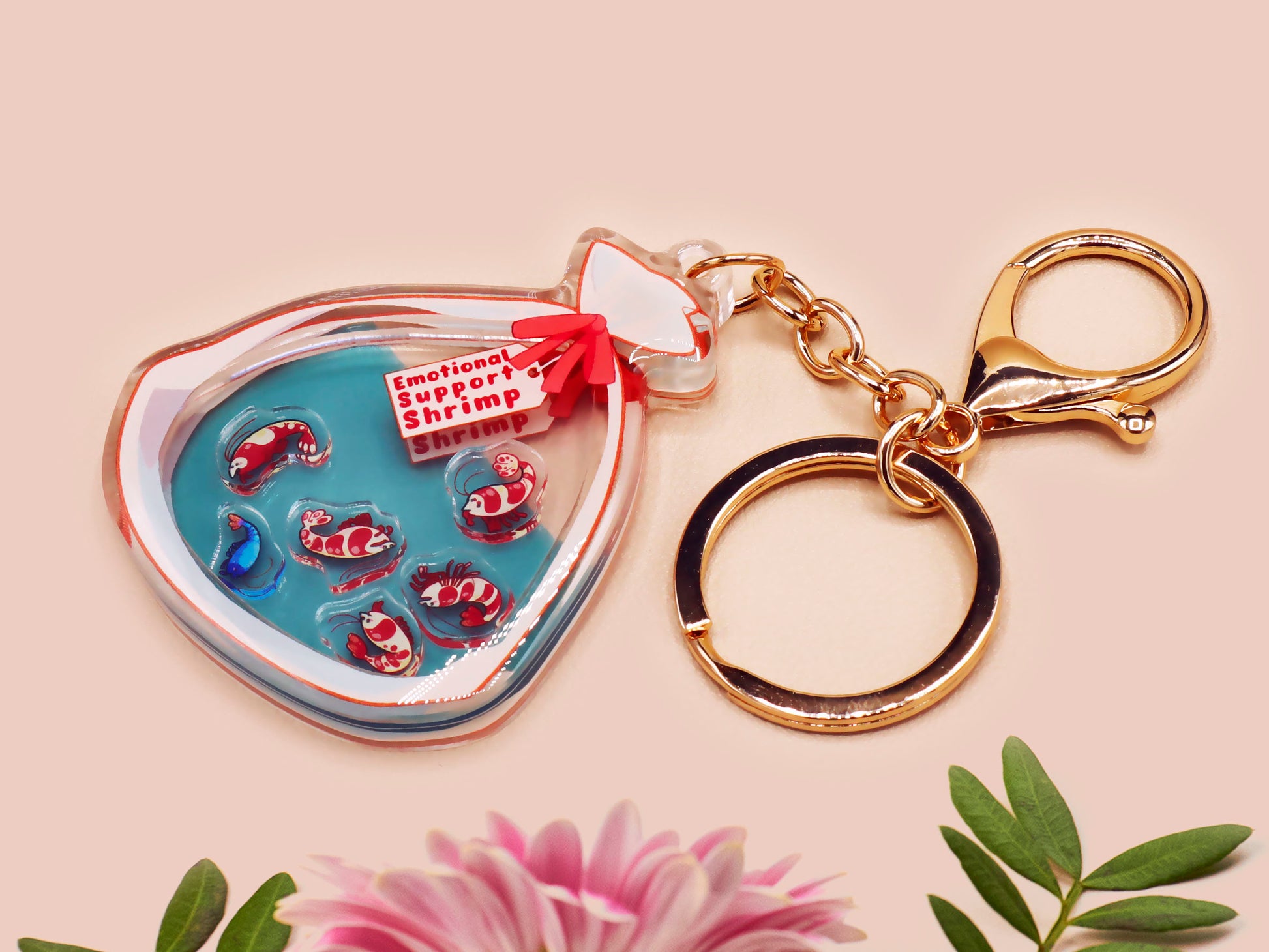 A large transparent acrylic shaker keychain with gold keyring, filled with mini chibi shrimps and labelled as emotional support shrimp