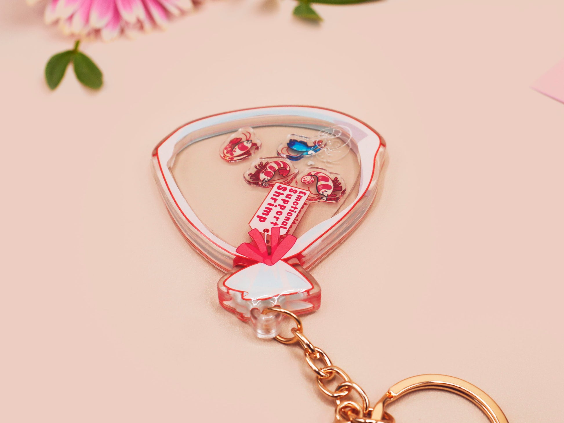 A large transparent acrylic shaker keychain with gold keyring, filled with mini chibi shrimps and labelled as emotional support shrimp