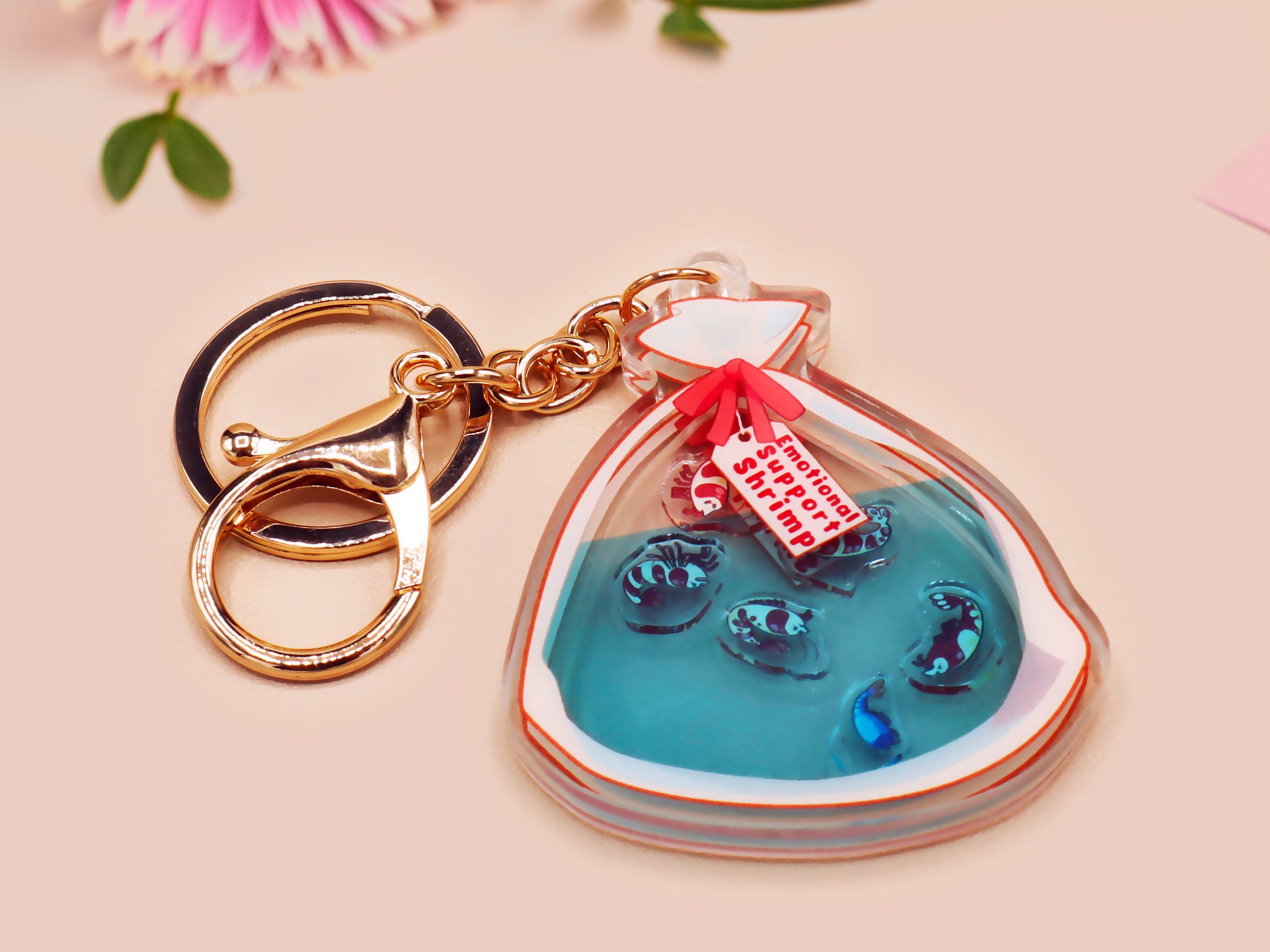 A large transparent acrylic shaker keychain with gold keyring, filled with mini chibi shrimps and labelled as emotional support shrimp