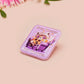 A clear acrylic pin badge with a pink heart-shaped pin back clasp. The design of the pin badge is of a cute chibi purple raccoon sat ona sofa wrapped in a blanket crying with the quote even baddies get saddies.