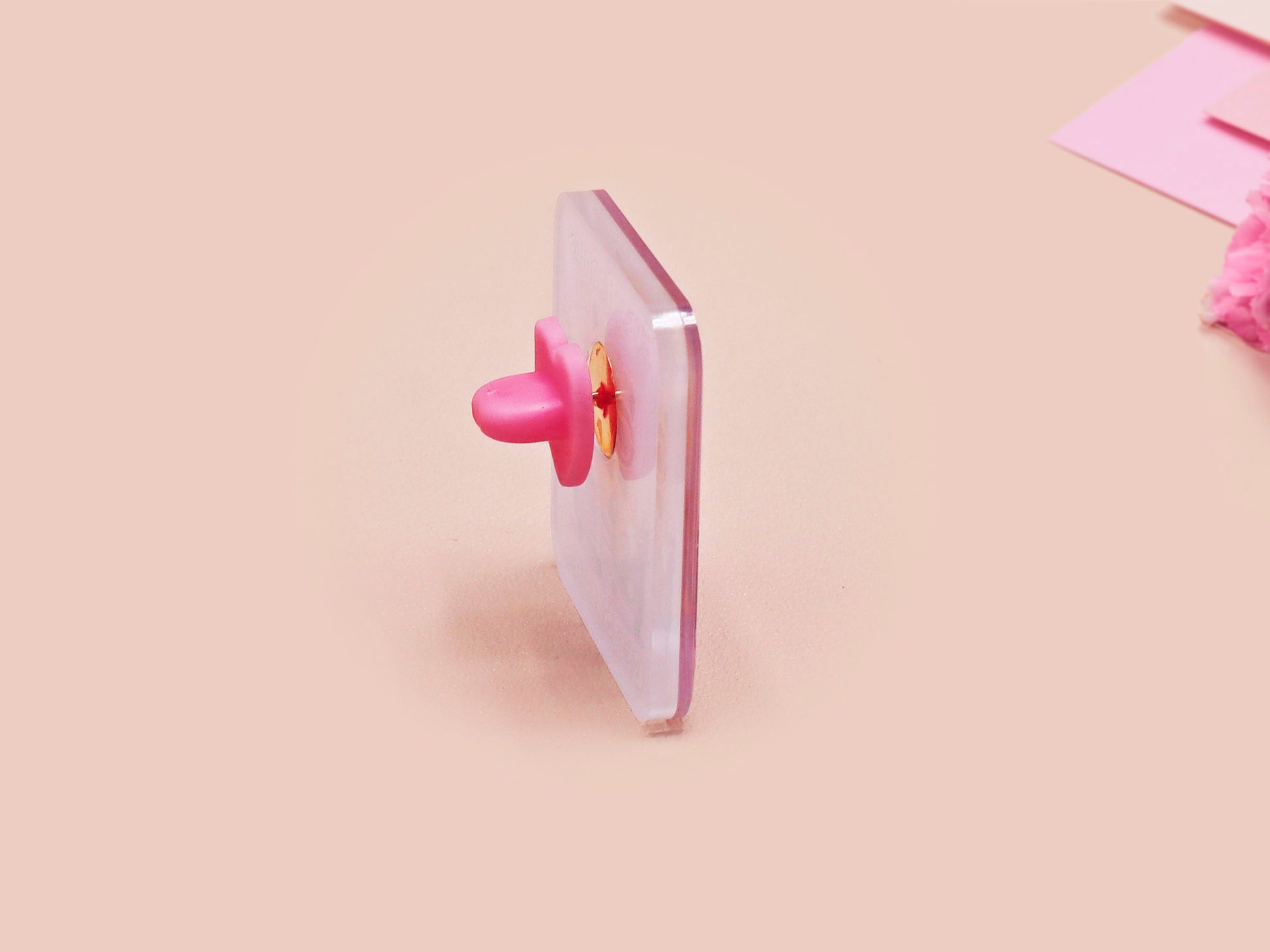 A clear acrylic pin badge with a pink heart-shaped pin back clasp. The design of the pin badge is of a cute chibi purple raccoon sat ona sofa wrapped in a blanket crying with the quote even baddies get saddies.