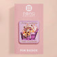 A clear acrylic pin badge with a pink heart-shaped pin back clasp. The design of the pin badge is of a cute chibi purple raccoon sat ona sofa wrapped in a blanket crying with the quote even baddies get saddies.
