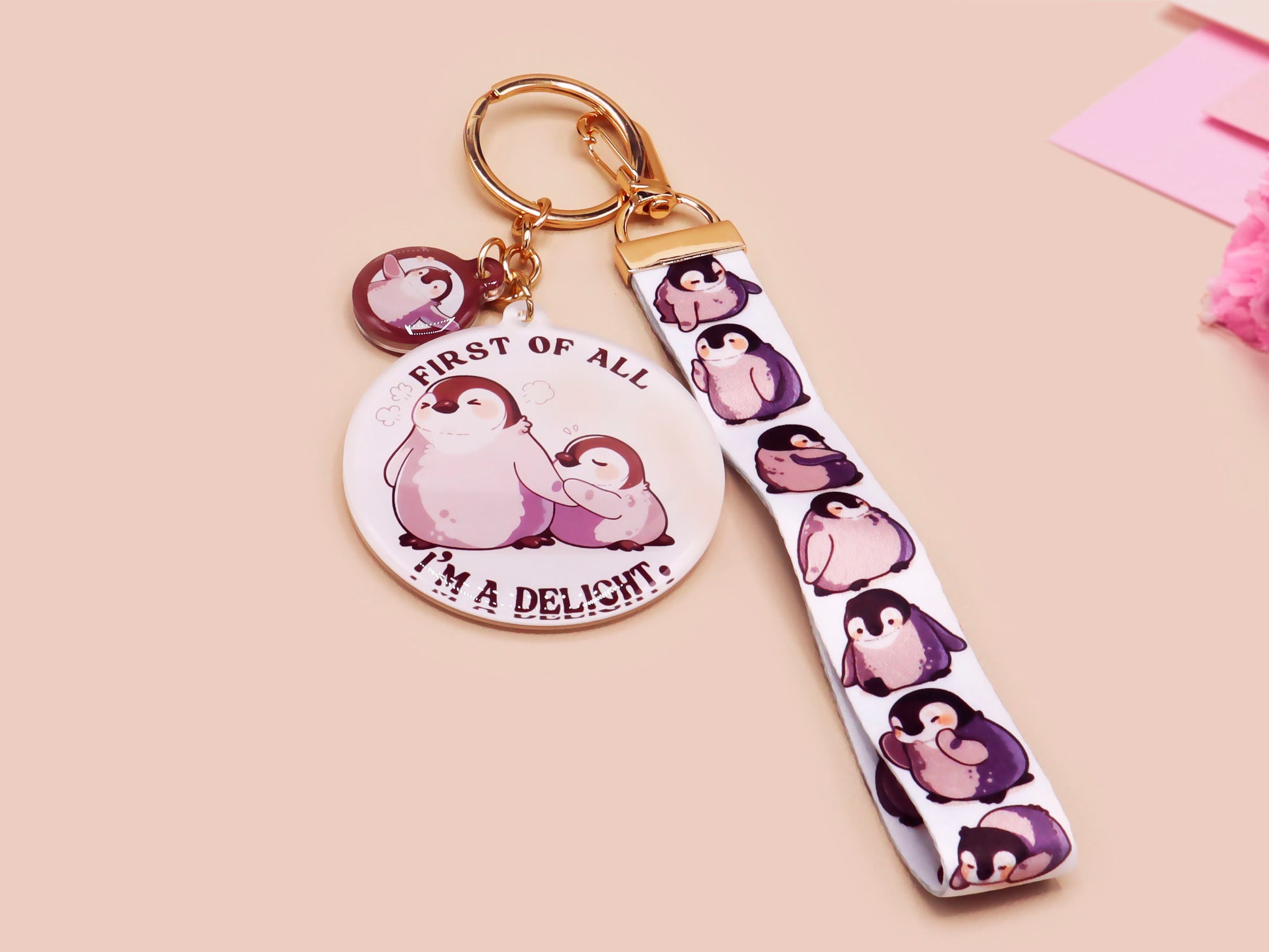 Acrylic epoxy baby penguin keychain with a large acrylic charm of two baby penguins with the quote first of all I'm a delight, a smaller charm of a cute penguin and a matching baby emperor penguin lanyard.