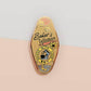 Gold Enamel Talisman Pin with yellow design and the words baker's Talisman, Baked With Love. The pins design includes a mixer and a rolling pin, moon water, as well as flowers and crystals.