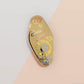 Gold Enamel Talisman Pin with yellow design and the words baker's Talisman, Baked With Love. The pins design includes a mixer and a rolling pin, moon water, as well as flowers and crystals.