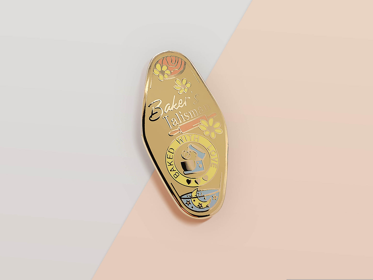 Gold Enamel Talisman Pin with yellow design and the words baker's Talisman, Baked With Love. The pins design includes a mixer and a rolling pin, moon water, as well as flowers and crystals.