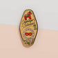 Gold Enamel Talisman Pin with yellow and red design and the words Cosplayer's Talisman, Places To Go People To Be. The pins design includes a mask and needle and thread, a wooden horse, as well as plants and crystals.