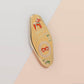 Gold Enamel Talisman Pin with yellow and red design and the words Cosplayer's Talisman, Places To Go People To Be. The pins design includes a mask and needle and thread, a wooden horse, as well as plants and crystals.