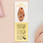 Gold Enamel Talisman Pin with pink design and the words Fandom Talisman sits on a long white and yellow backing card with gold accents. The backing card has details the symbolism of the different design elements of the Talisman pin.