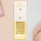 The back of the long white and yellow backing card with gold accents. The backing card details the symbolism of the different design elements of the Fandom Talisman pin. Also shown is the two gold locking pin backs attached to the card.