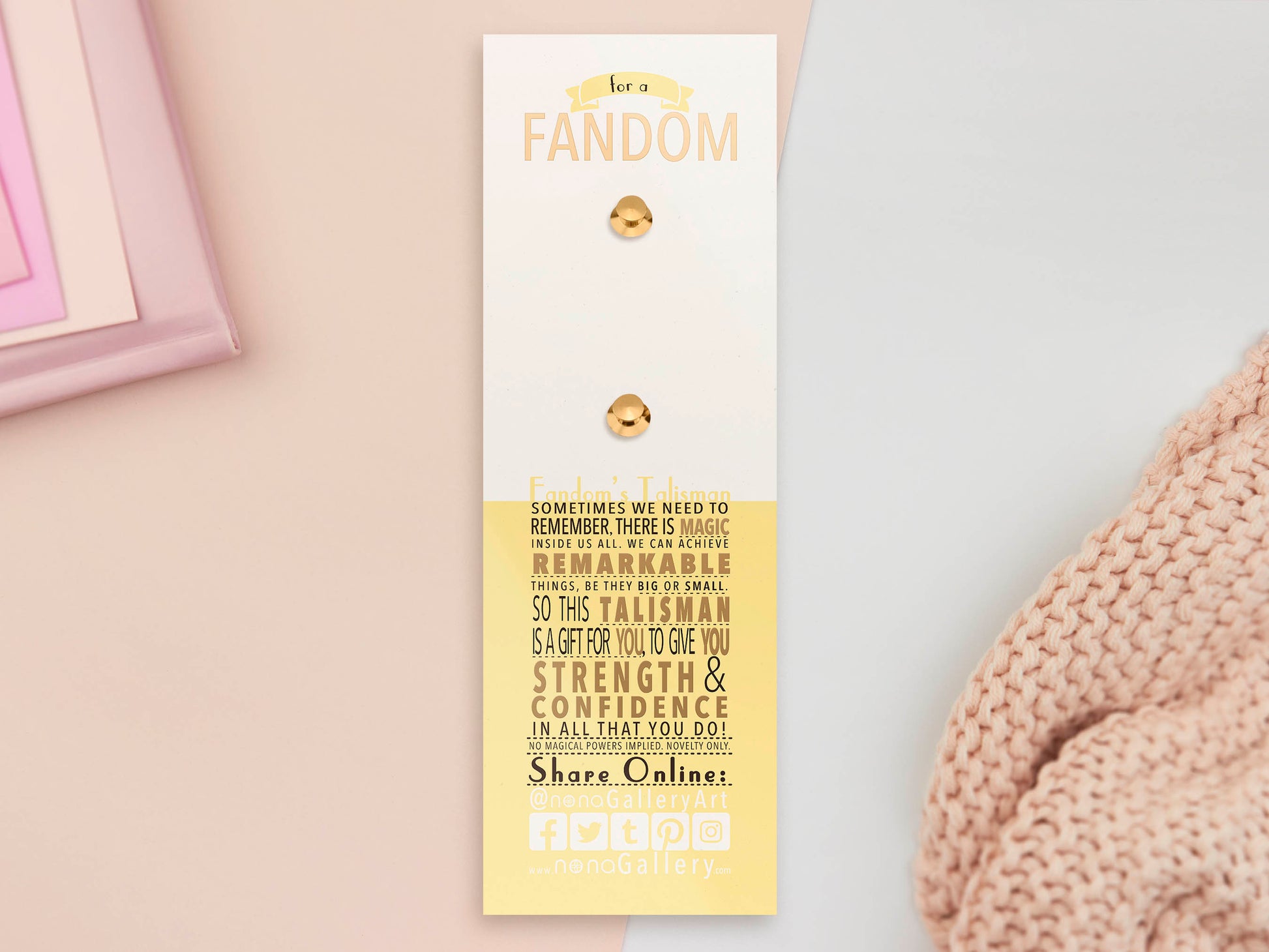 The back of the long white and yellow backing card with gold accents. The backing card details the symbolism of the different design elements of the Fandom Talisman pin. Also shown is the two gold locking pin backs attached to the card.