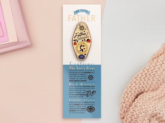 Gold Enamel Talisman Pin with yellow design and the words Father's Talisman sits on a long white and blue backing card with gold accents. The backing card has details the symbolism of the different design elements of the Talisman pin.