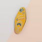 Gold Enamel Talisman Pin with yellow design and the words Gamer's Talisman, May Your Progress Always Save. The pins design includes a game console controller and health hearts, A jin Chan money toad, as well as plants and crystals.
