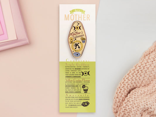 Gold Enamel Talisman Pin with yellow design and the words Mother's Talisman sits on a long white and green backing card with gold accents. The backing card has details the symbolism of the different design elements of the Talisman pin.