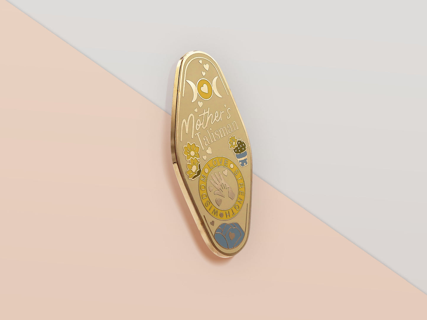 Gold Enamel Talisman Pin with yellow design and the words Mother's Talisman, Wisdom Love Strength. The pins design includes a a mother and child's hand, the three mothers moons, as well as flowers and crystals.