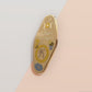 Gold Enamel Talisman Pin with yellow design and the words Mother's Talisman, Wisdom Love Strength. The pins design includes a a mother and child's hand, the three mothers moons, as well as flowers and crystals.