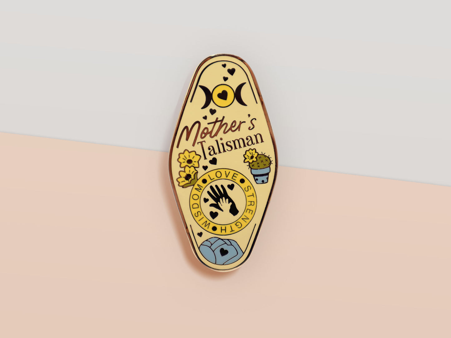 Gold Enamel Talisman Pin with yellow design and the words Mother's Talisman, Wisdom Love Strength. The pins design includes a a mother and child's hand, the three mothers moons, as well as flowers and crystals.
