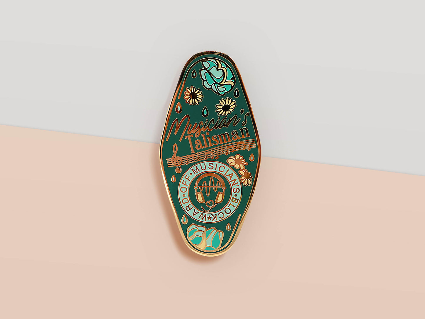 Gold Enamel Talisman Pin with blue design and the words Musician's Talisman, Ward of Musician's block. The pins design includes headphones and sheet music, raindrops, as well as flowers and crystals.