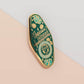 Gold Enamel Talisman Pin with blue design and the words Musician's Talisman, Ward of Musician's block. The pins design includes headphones and sheet music, raindrops, as well as flowers and crystals.