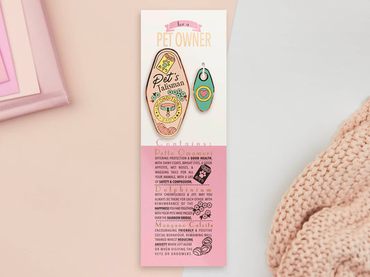 Gold Enamel Talisman Pin with mini charm and the words Pet Owner's Talisman sits on a long white and pink backing card with gold accents. The backing card has details the symbolism of the different design elements of the Talisman pin.