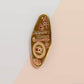 Gold Enamel Talisman Pin with brown design and the words Photographer's Talisman, Ward of bad lighting. The pins design includes a camera and a film, a red bird, as well as flowers and crystals.