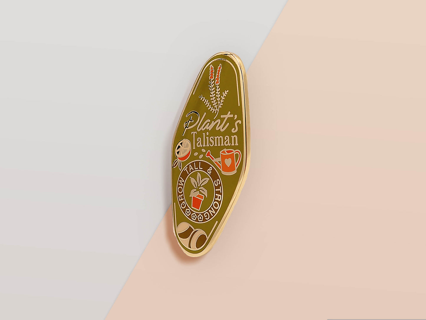 Gold Enamel Talisman Pin with green design and the words plant's Talisman, grow tall and strong. The pins design includes a potted plant and a watering can, fruit, as well as flowers and crystals.