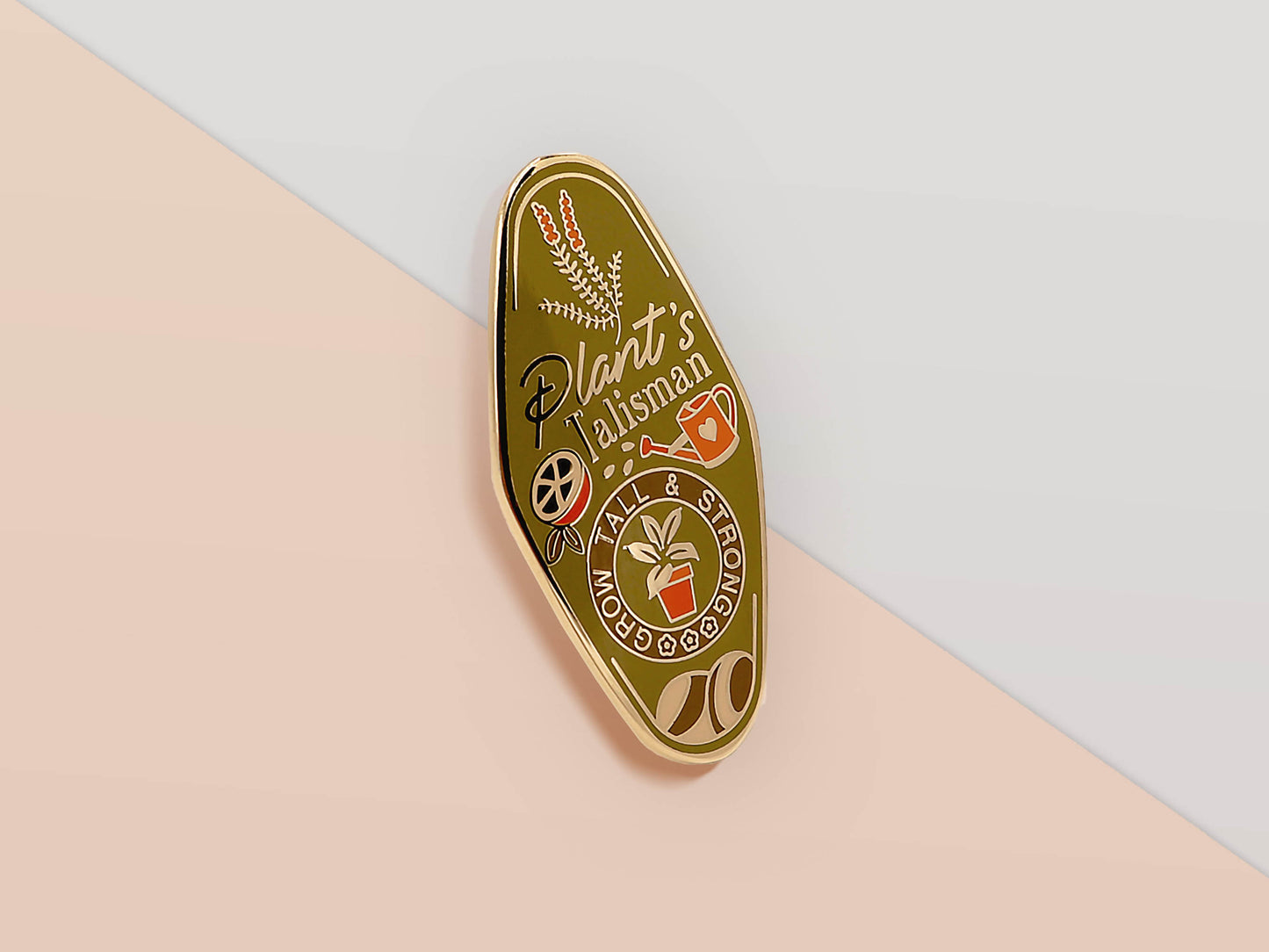 Gold Enamel Talisman Pin with green design and the words plant's Talisman, grow tall and strong. The pins design includes a potted plant and a watering can, fruit, as well as flowers and crystals.