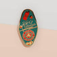 Gold Enamel Talisman Pin with red and blue design and the words RPG Talisman, Let Your Adventure Begin. The pins design includes a D20 dice and a sword and pencil, Hongbao red envelope, as well as acorns and crystals.