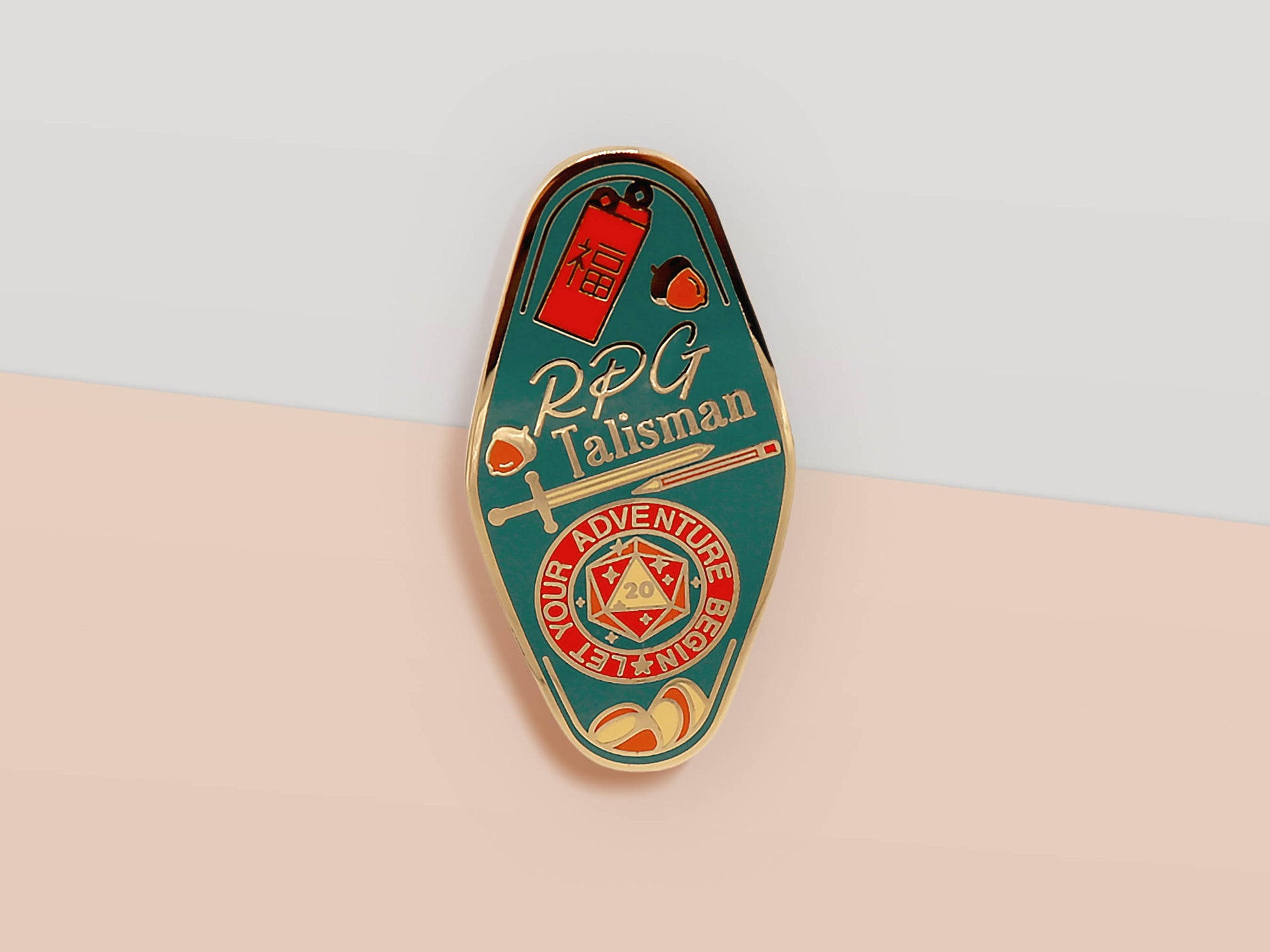 Gold Enamel Talisman Pin with red and blue design and the words RPG Talisman, Let Your Adventure Begin. The pins design includes a D20 dice and a sword and pencil, Hongbao red envelope, as well as acorns and crystals.