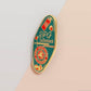 Gold Enamel Talisman Pin with red and blue design and the words RPG Talisman, Let Your Adventure Begin. The pins design includes a D20 dice and a sword and pencil, Hongbao red envelope, as well as acorns and crystals.