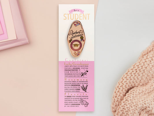 Gold Enamel Talisman Pin with white design and the words Student's Talisman sits on a long white and pink backing card with gold accents. The backing card has details the symbolism of the different design elements of the Talisman pin.