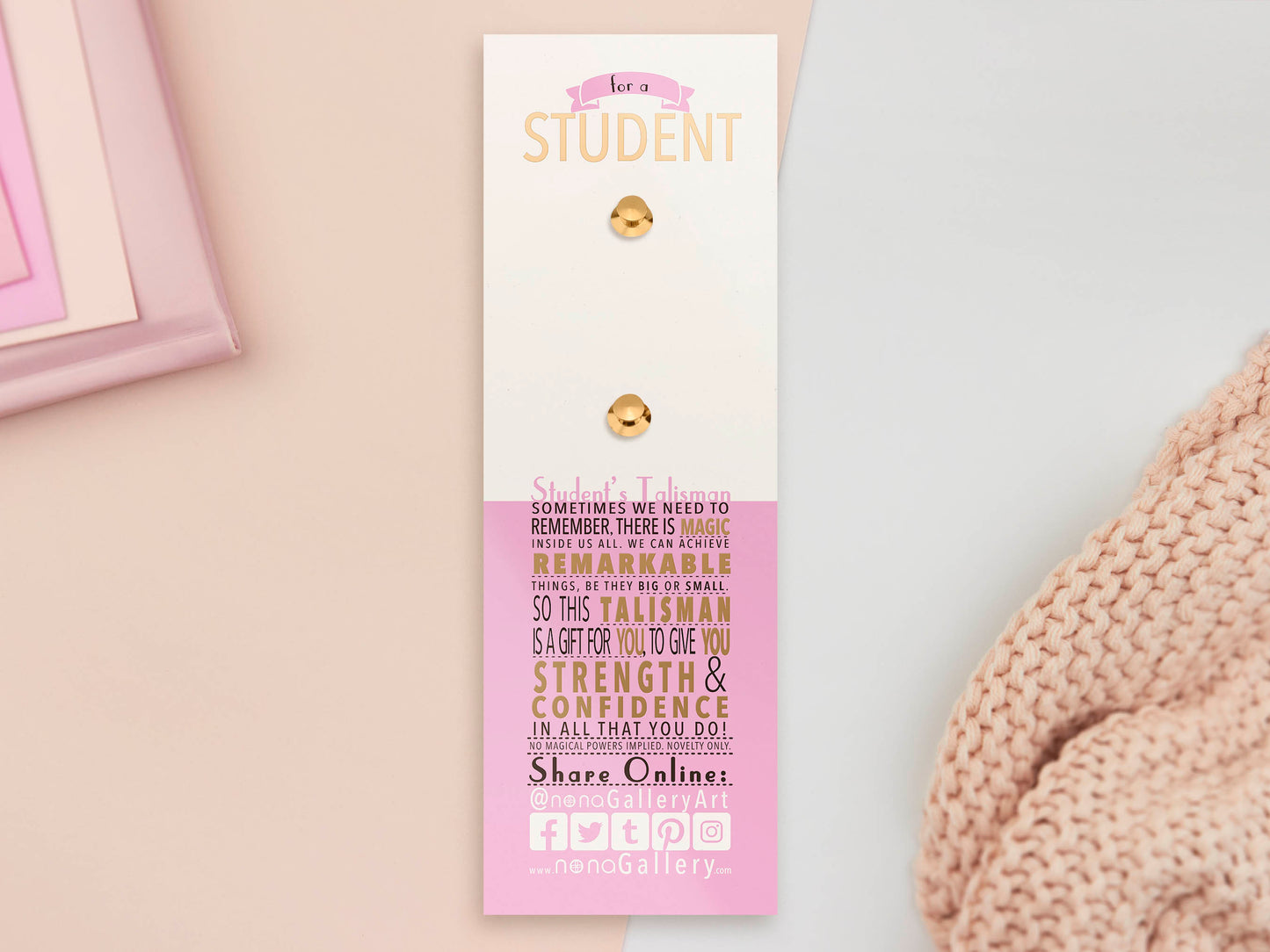 The back of the long white and pink backing card with gold accents. The backing card details the symbolism of the different design elements of the Student's Talisman pin. Also shown is the two gold locking pin backs attached to the card.
