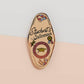 Gold Enamel Talisman Pin with white design and the words Student's Talisman, Ward of procrastination. The pins design includes a graduation cap and a rosette, a grass hopper, as well as plants and crystals.