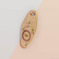 Gold Enamel Talisman Pin with white design and the words Student's Talisman, Ward of procrastination. The pins design includes a graduation cap and a rosette, a grass hopper, as well as plants and crystals.