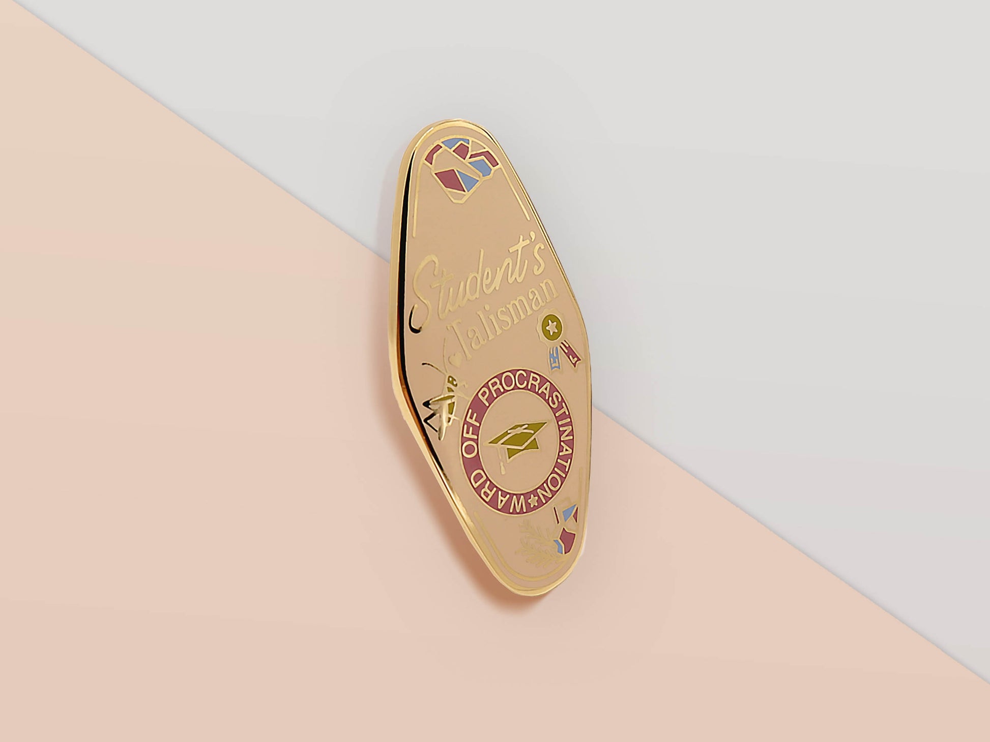 Gold Enamel Talisman Pin with white design and the words Student's Talisman, Ward of procrastination. The pins design includes a graduation cap and a rosette, a grass hopper, as well as plants and crystals.