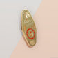 Gold Enamel Talisman Pin with green design and the words Teacher's Talisman, Helping Them Grow. The pins design includes a stack of books and an apple, a barn owl, as well as plants, flowers and crystals.