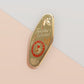 Gold Enamel Talisman Pin with green design and the words Teacher's Talisman, Helping Them Grow. The pins design includes a stack of books and an apple, a barn owl, as well as plants, flowers and crystals.