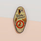 Gold Enamel Talisman Pin with green design and the words Teacher's Talisman, Helping Them Grow. The pins design includes a stack of books and an apple, a barn owl, as well as plants, flowers and crystals.