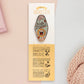 Gold Enamel Talisman Pin with blue design and the words Writer's Talisman sits on a long white and yellow backing card with gold accents. The backing card has details the symbolism of the different design elements of the Talisman pin.