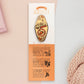 Gold Enamel Talisman Pin with yellow design and the words Artist's Talisman sits on a long white and orange backing card with gold accents. The backing card has details the symbolism of the different design elements of the Talisman pin.