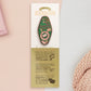 A Bookworm's Talisman gold enamel pin on a gold foiled backing card that outlines the symbolism of the talisman including information and imagery on double shooting stars, sage leaves and brecciated jasper.