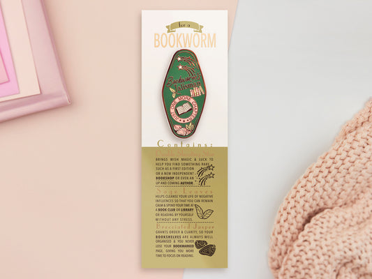 A Bookworm's Talisman gold enamel pin on a gold foiled backing card that outlines the symbolism of the talisman including information and imagery on double shooting stars, sage leaves and brecciated jasper.