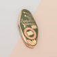 A Bookworm's Talisman gold enamel pin on a gold foiled backing card that outlines the symbolism of the talisman including information and imagery on double shooting stars, sage leaves and brecciated jasper.