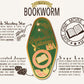 A detailed illustration outlining the symbolism of the Bookworms's Talisman gold enamel pin on a gold foiled backing card that outlines the symbolism of the talisman