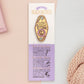 A Health Worker's Talisman gold enamel pin on a gold foiled backing card that outlines the symbolism of the talisman including information and imagery on the Rod of Asclepius, Lavender Stems and Prehnite Crystals